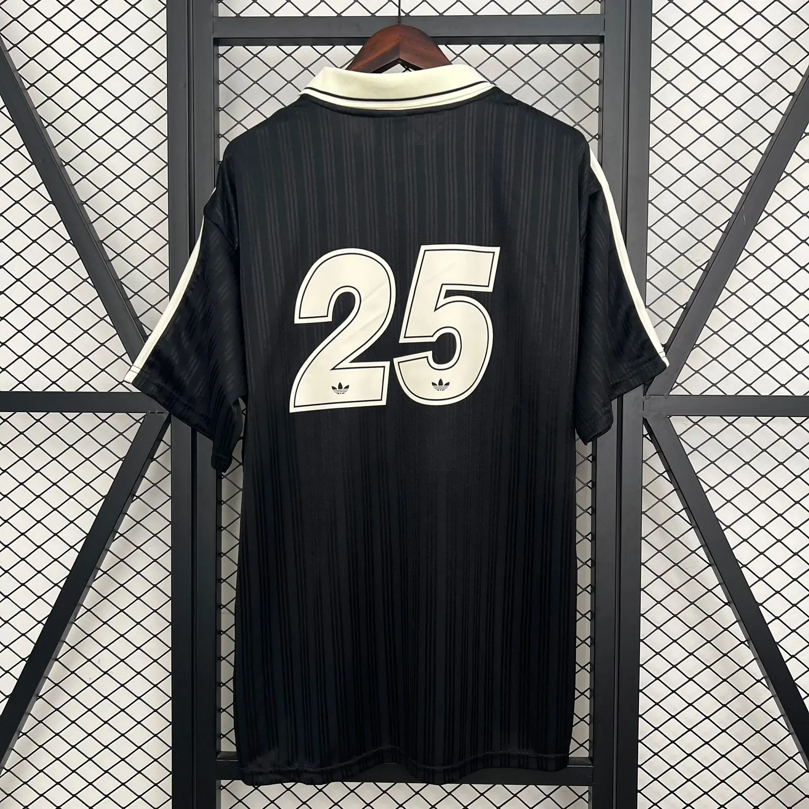 Camiseta negra estilo jersey de fútbol de la banda Oasis Live 25 con cuello polo crema, tres tiras en hombros y escudo conmemorativo.