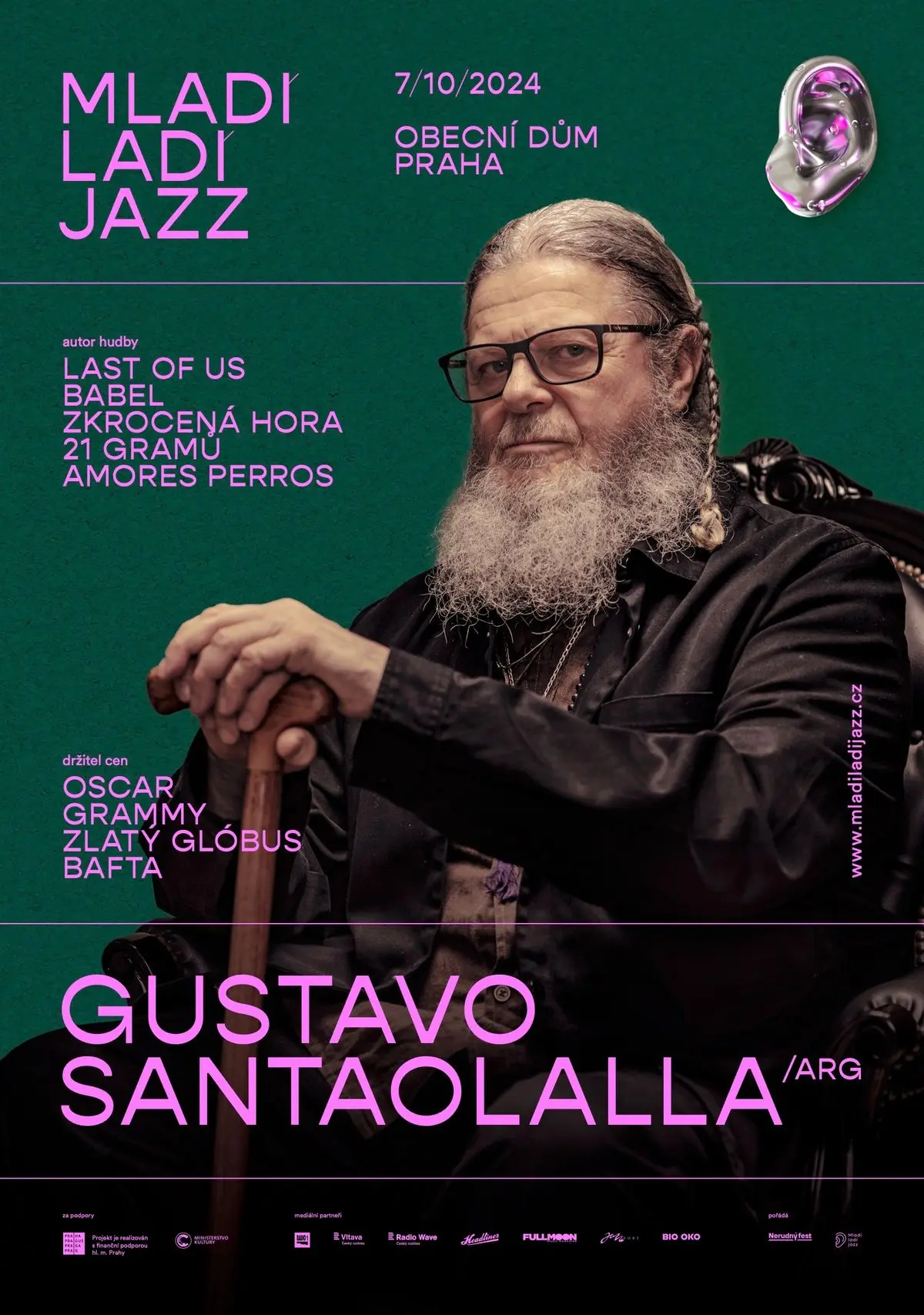 Retablo decorativo de madera colgado en una pared blanca con el póster oficial del concierto de Gustavo Santaolalla en el festival Mladi Ladi Jazz Praga, mostrando un fondo verde y letras rosadas.